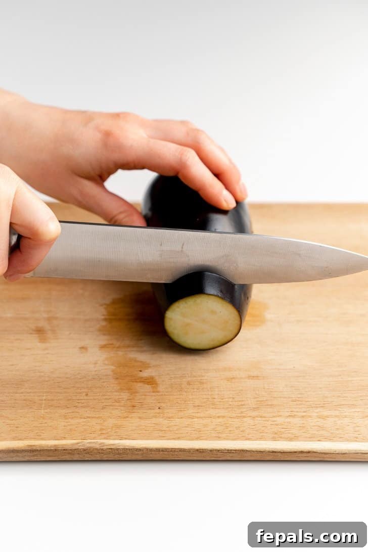 Slicing Eggplant into Uniform Rounds Chef's knife carefully slicing an eggplant into circular rounds.