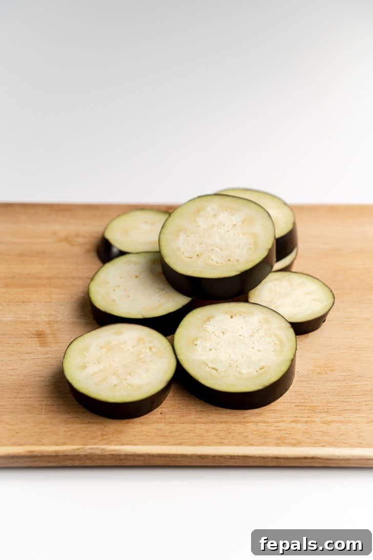 Stack of Fresh Eggplant Rounds A stack of freshly cut eggplant rounds on a cutting board.