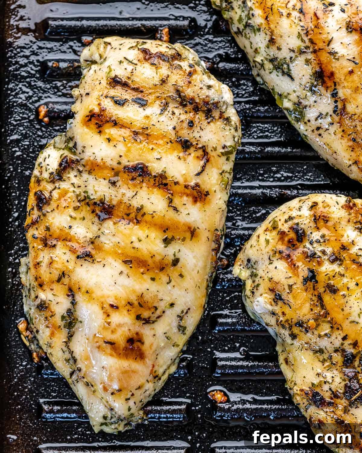 Two pieces of seasoned chicken breast searing on a hot black grill pan, showing initial grill marks.