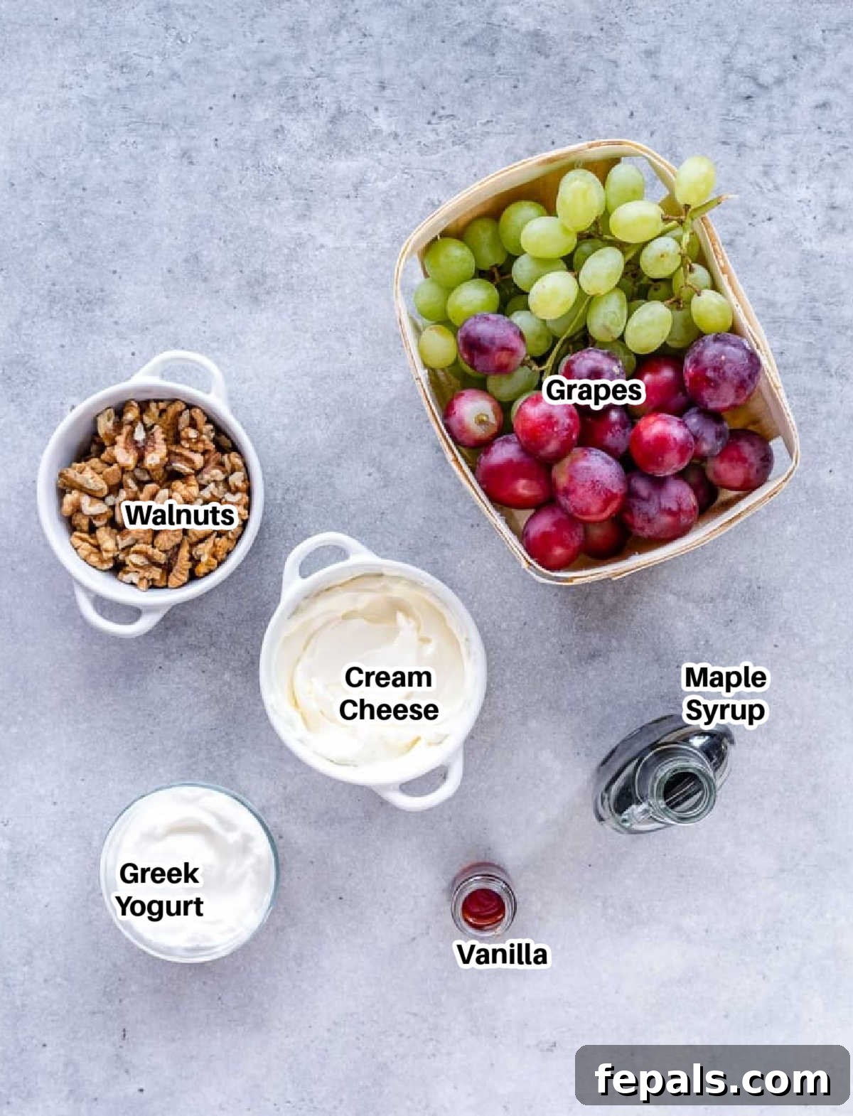 A vibrant display of fresh ingredients for grape salad including colorful grapes, walnuts, cream cheese, Greek yogurt, maple syrup, and vanilla extract.