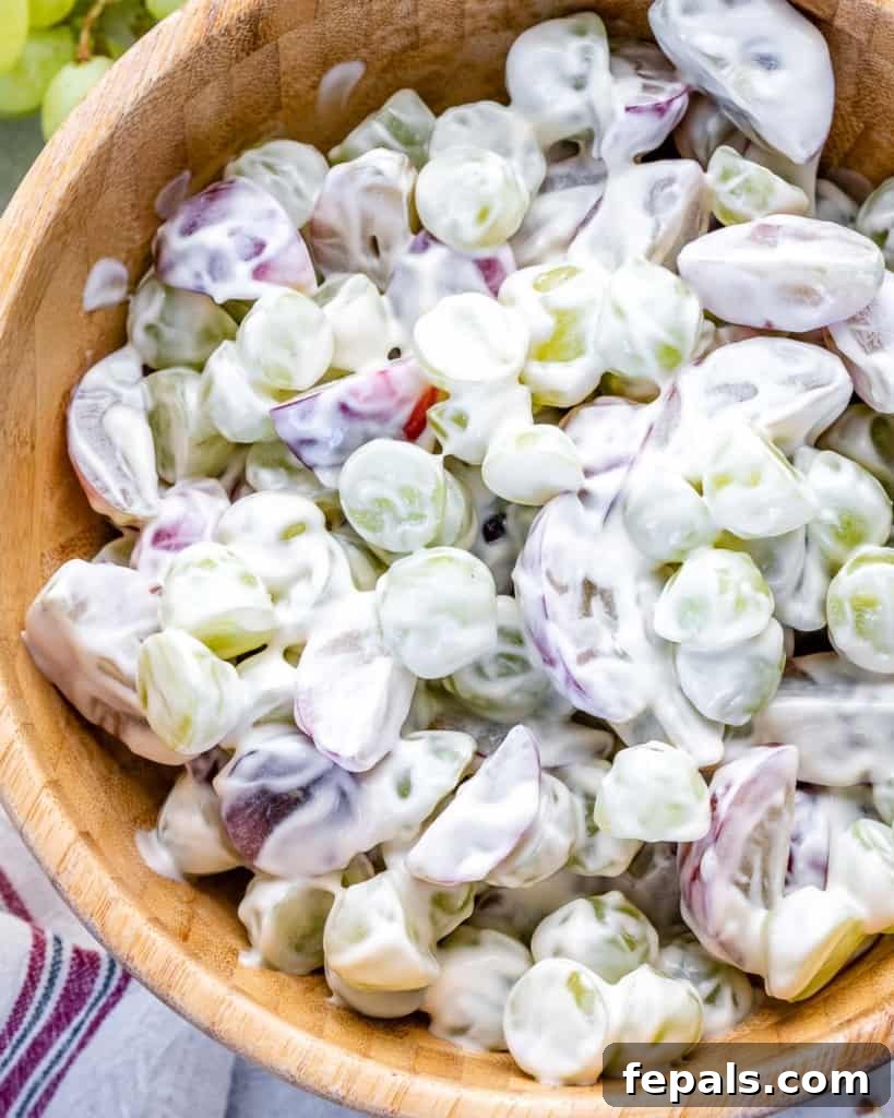 Sliced grapes coated in a creamy yogurt and cream cheese dressing, mixing thoroughly in a wooden bowl.