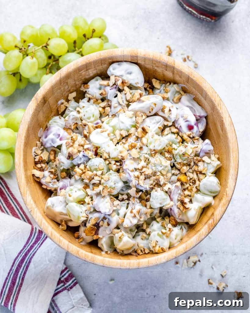Close-up top view of grape salad with yogurt dressing and walnuts in a brown bowl, showcasing the creamy texture and crunchy topping.