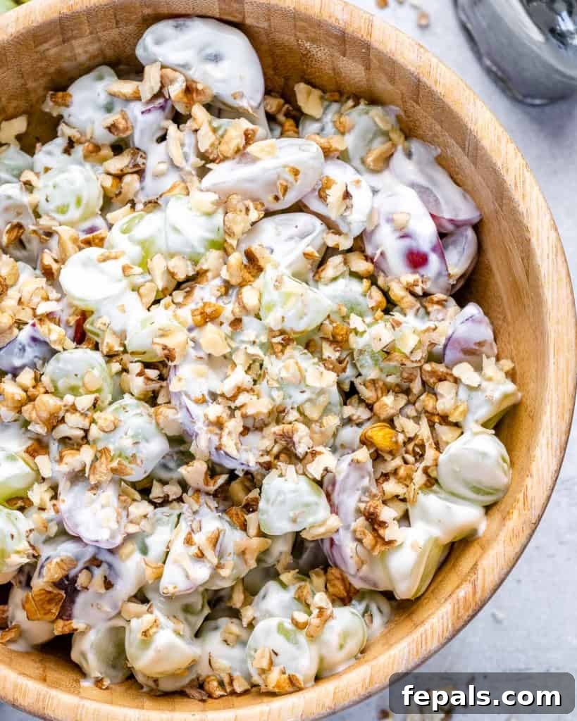 Top view of a beautifully presented creamy grape salad in a round wooden bowl, garnished with crushed walnuts, ready to be enjoyed.