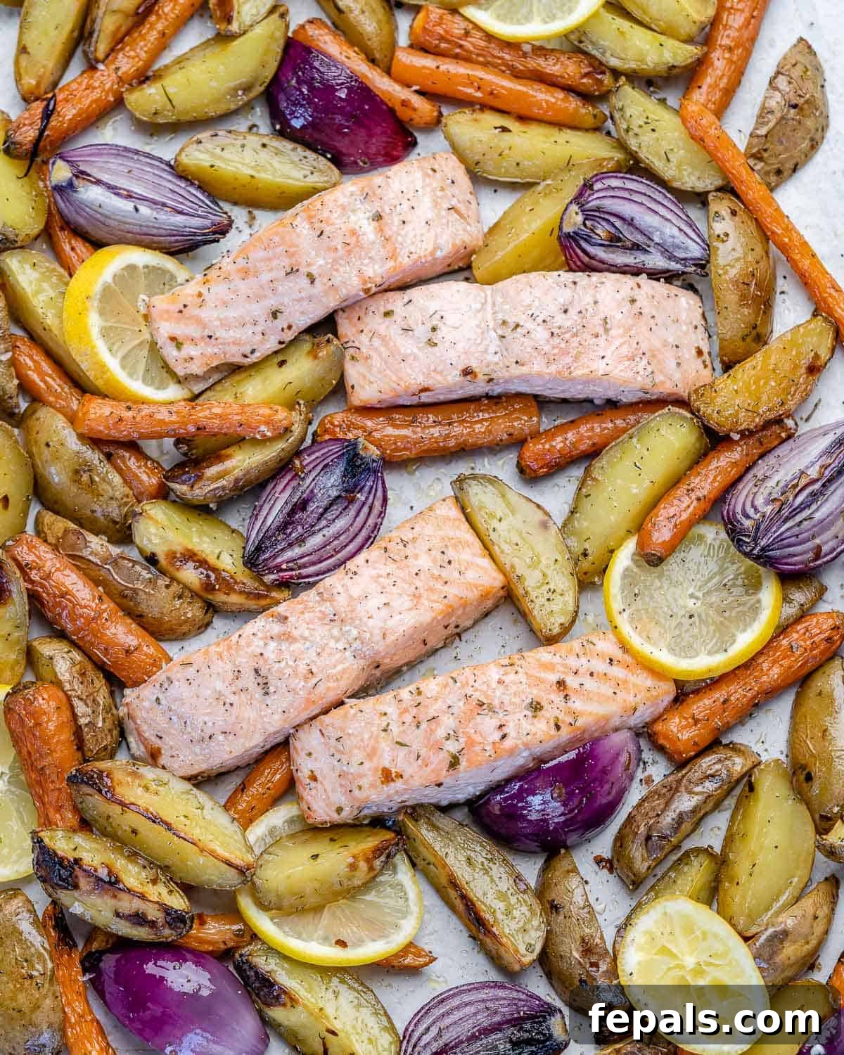 Freshly baked salmon fillets with roasted baby potatoes and carrots, garnished with lemon slices and herbs, ready to serve.