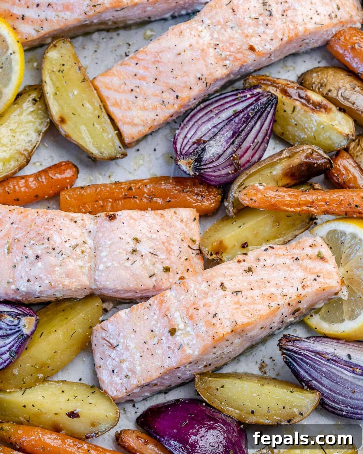 Close-up view of perfectly oven-baked salmon fillets nestled among tender roasted vegetables and potatoes on a baking sheet.