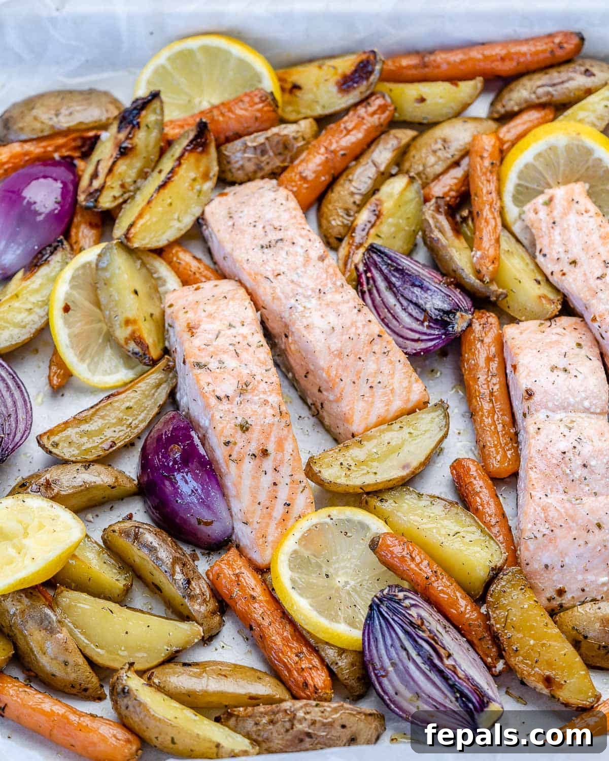 Top-down view of a completed oven-roasted salmon dish with potatoes and mixed vegetables arranged neatly on a baking tray.