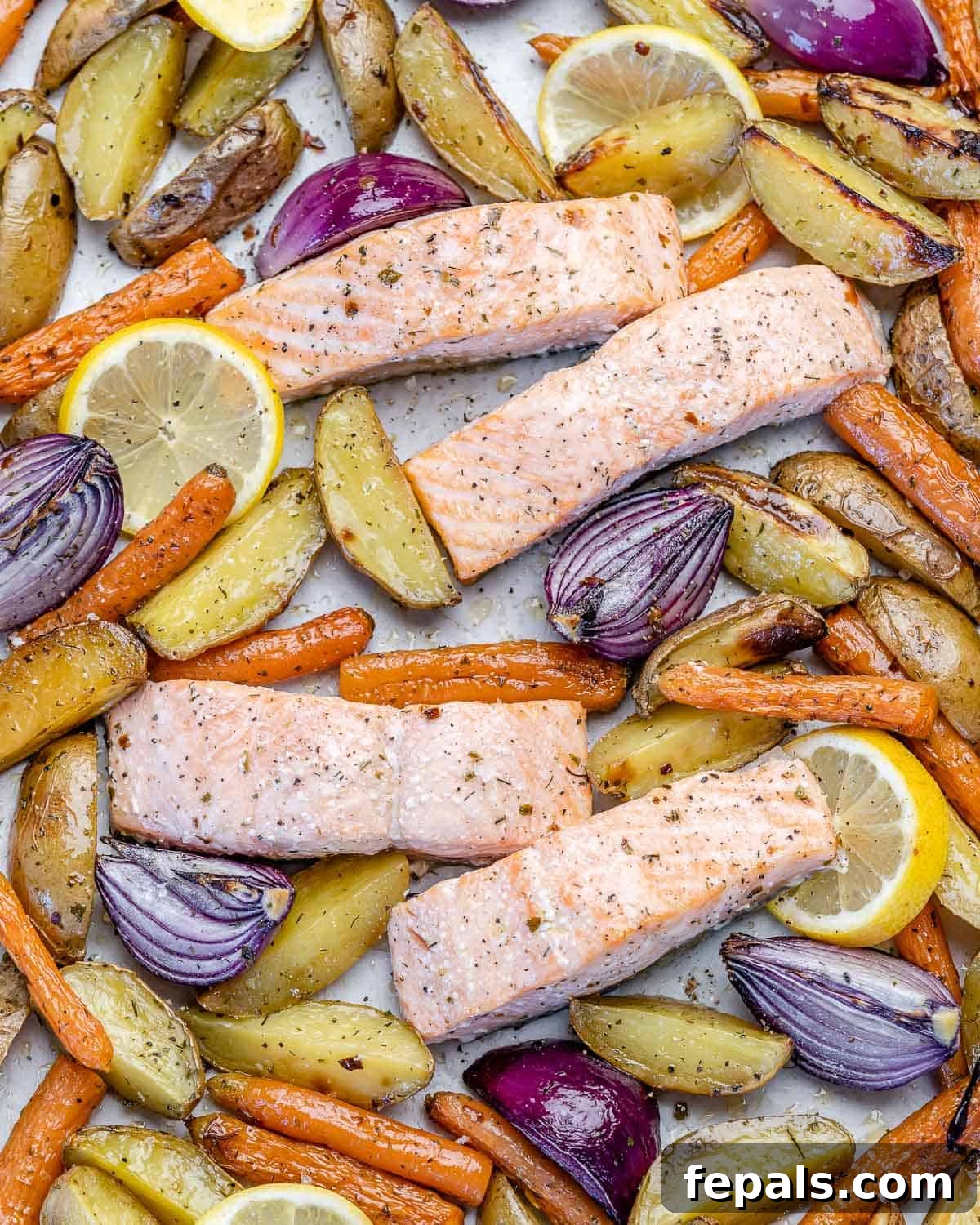 Four perfectly baked salmon fillets on a baking sheet, surrounded by golden roasted potatoes and tender mixed vegetables, ready to be served.