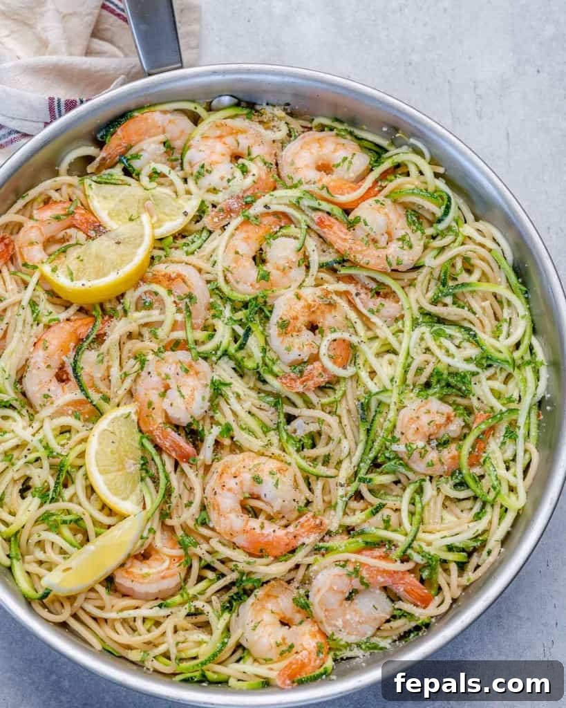 Zesty Lemon Shrimp Pasta with Zucchini Noodles 8 A close-up view of a single serving of lemon garlic shrimp pasta with zoodles, topped with grated parmesan cheese and a lemon wedge, on a white plate.