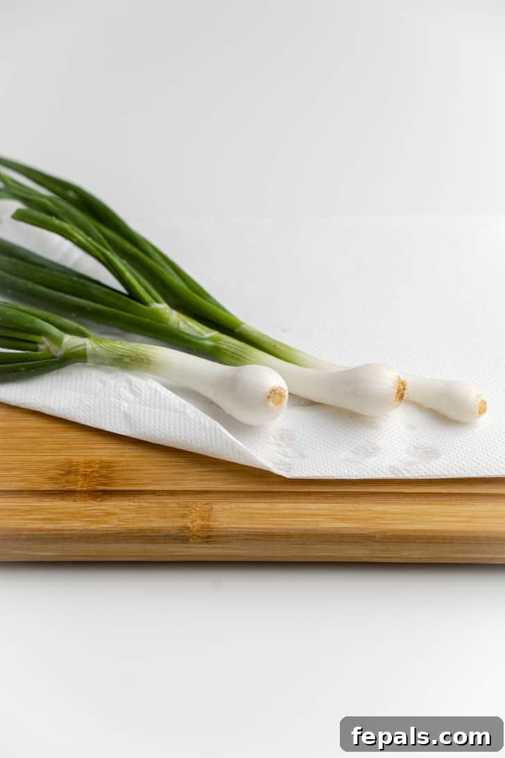 Three green onions drying on a wooden cutting board alongside paper towels to absorb moisture