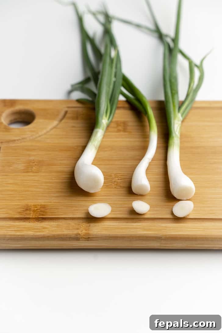 Three trimmed scallions arranged neatly on a wooden cutting board, ready for slicing