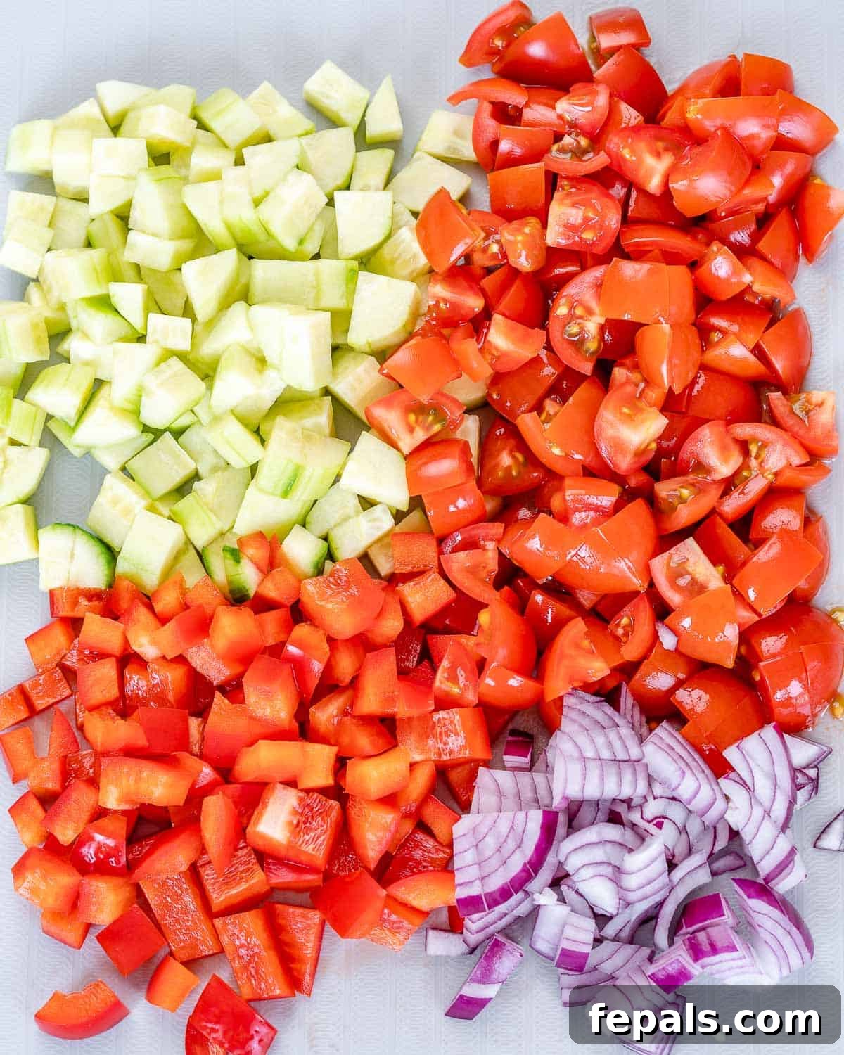 Greek Quinoa Salad With Feta Cheese Preparation Chopped red onions, tomatoes, and cucumbers ready on a cutting board