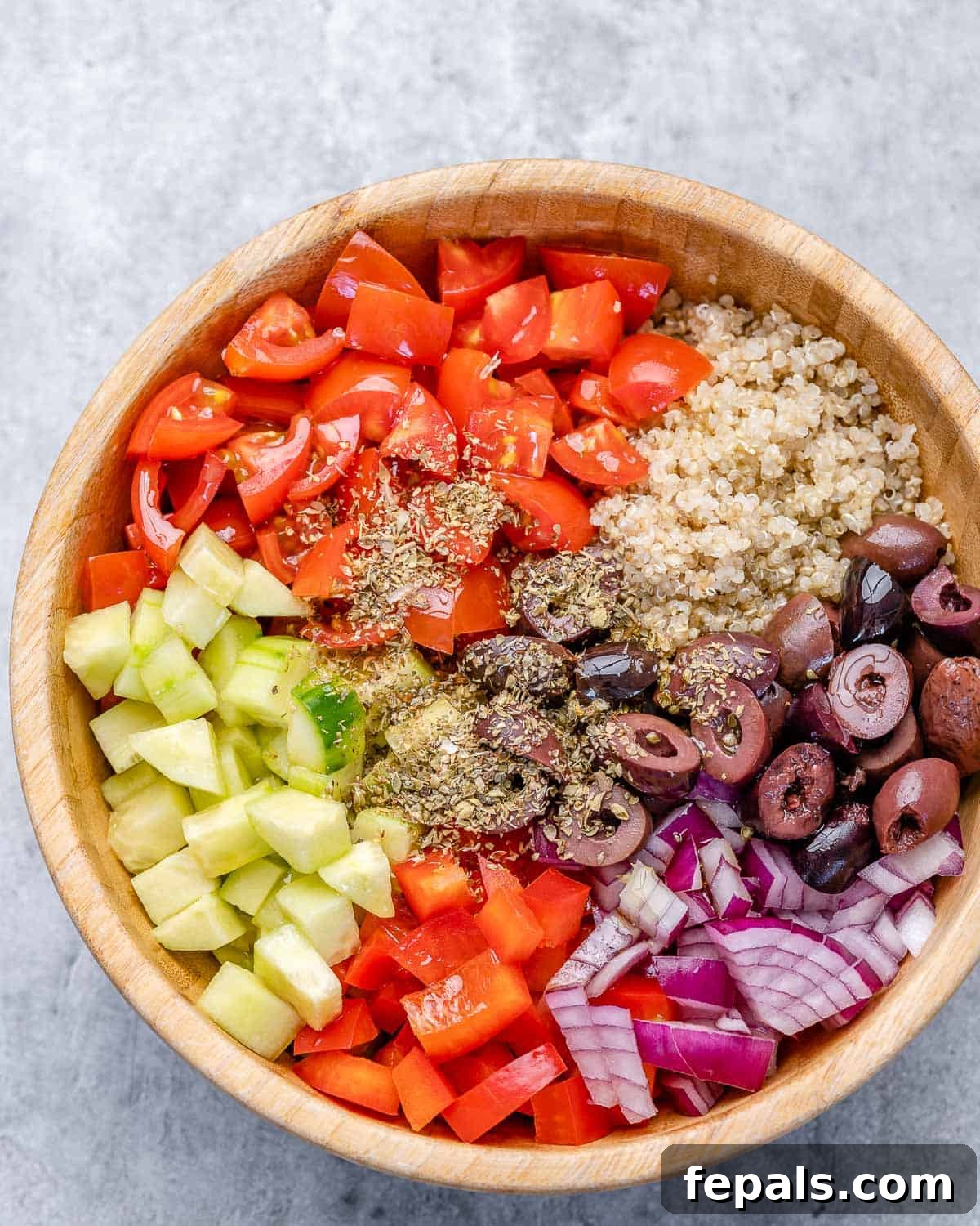 Combining Ingredients for Greek Quinoa Salad Cucumbers, tomatoes, red onion, kalamata olives, and cooked quinoa with oregano in a large mixing bowl