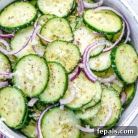 cucumber salad in a white bowl with thinly sliced cucumbers and red onions.