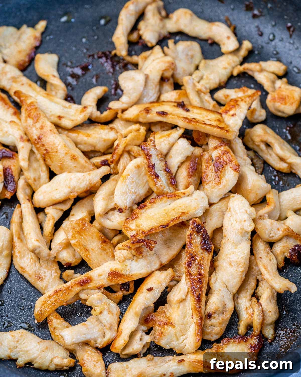 Close-up view of sliced chicken pieces cooking in a hot skillet, browning beautifully as they absorb the marinade.