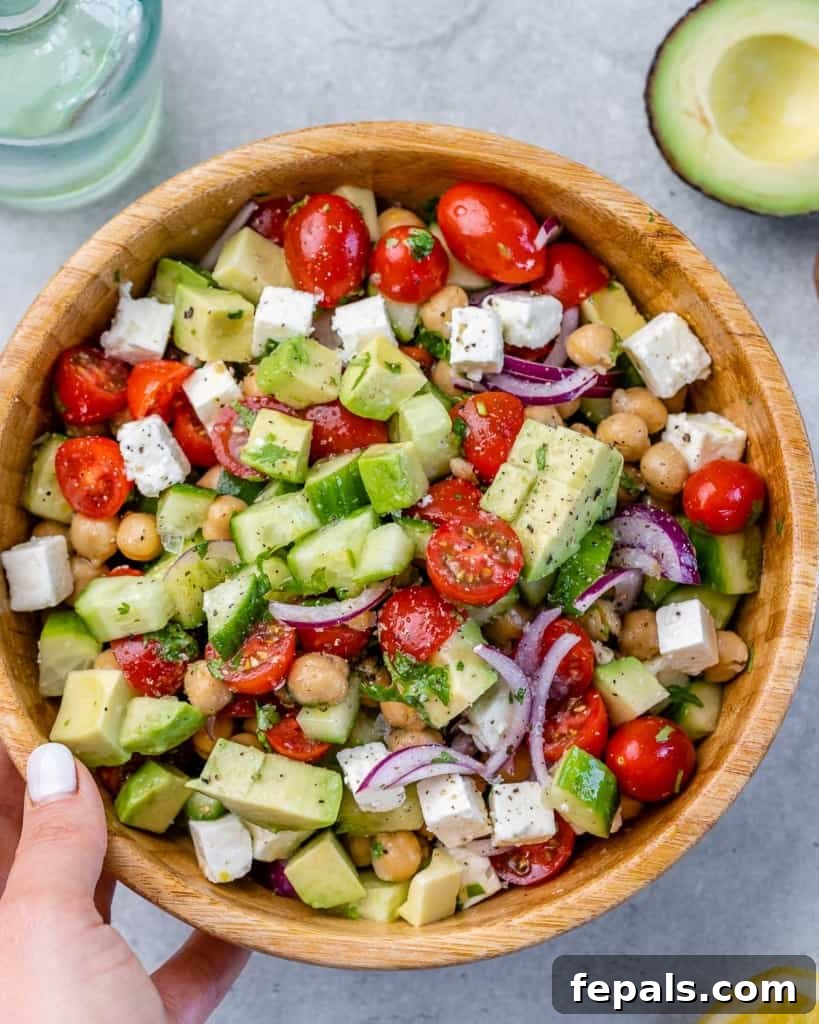 hand holding brown bowl of greek chickpea feta salad 