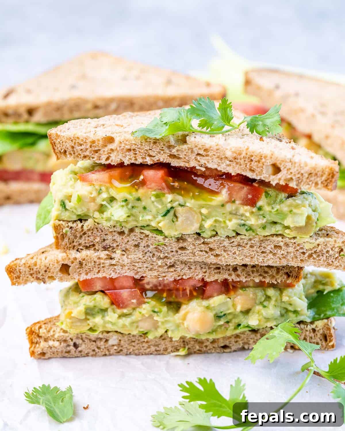Avocado Chickpea Sandwich A chickpea avocado sandwich served open-faced on bread with tomato slices, ready to be enjoyed.