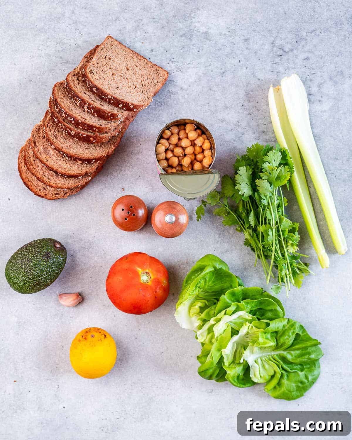 Smashed Chickpea Sandwich Arrangement of fresh ingredients: bread slices, canned chickpeas, celery, cilantro, lettuce, tomato, lemon, garlic, and avocado.