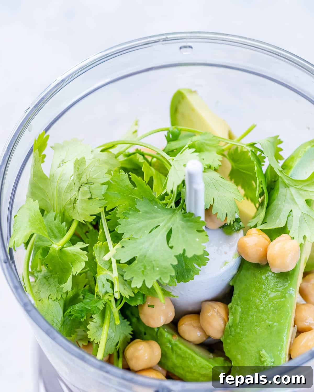 Smashed Avocado Chickpea Sandwich Recipe A food processor bowl with chickpeas, avocado, lemon, cilantro, and garlic, ready to be pulsed.