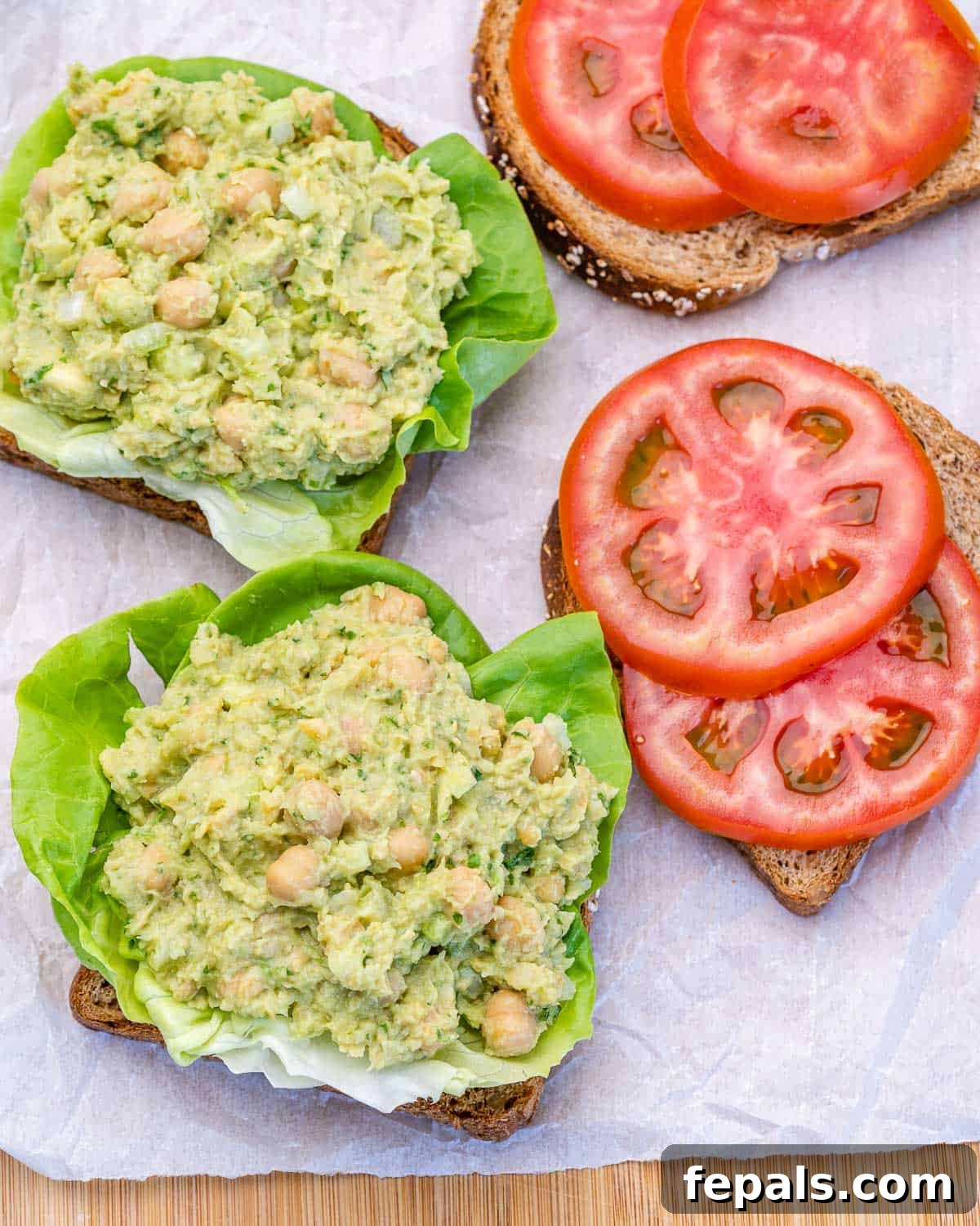 Smashed Chickpea Sandwich An open chickpea avocado sandwich with lettuce and tomato slices on bread, ready to be closed.