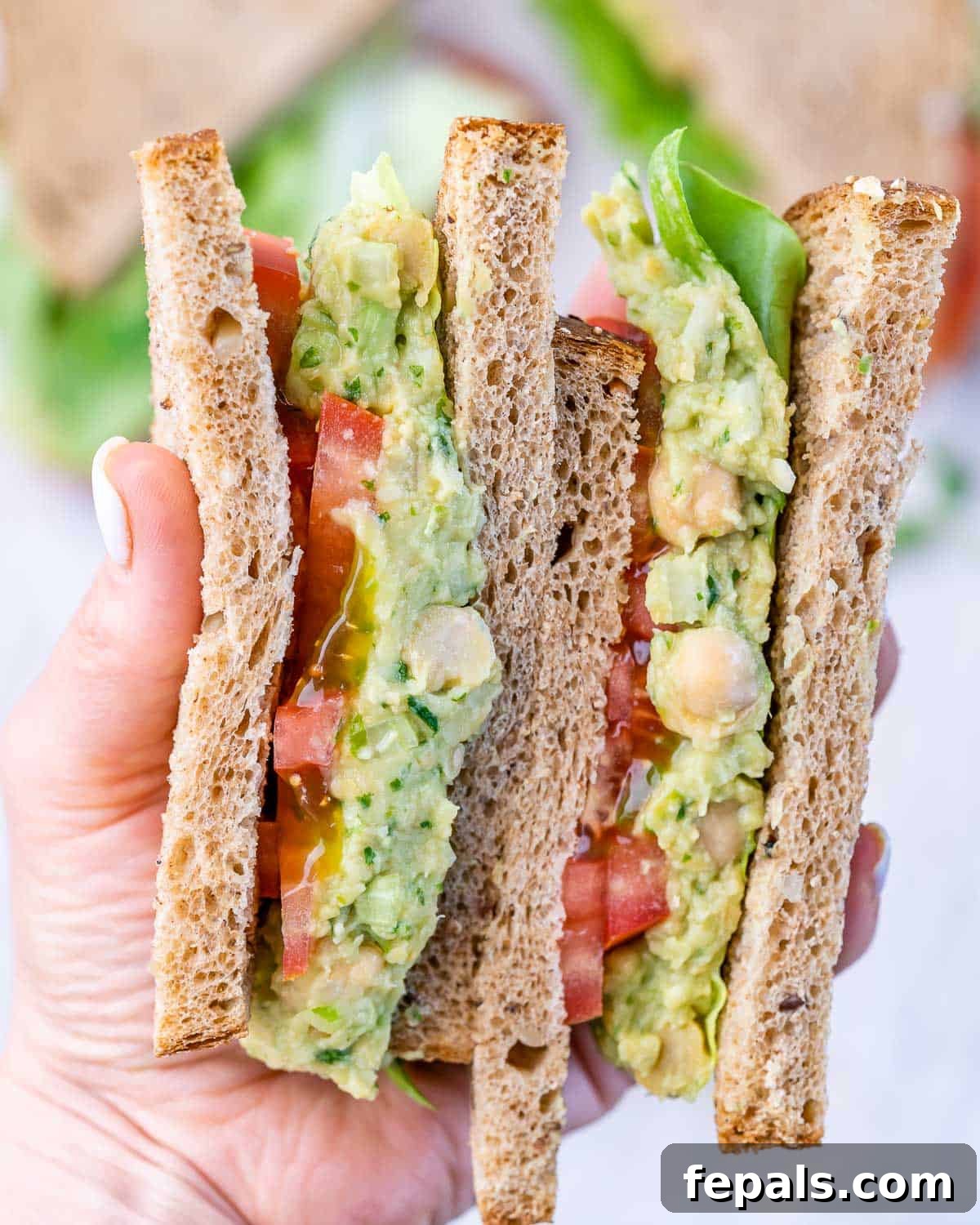 Smashed Avocado Chickpea Sandwich Front view of a perfectly assembled chickpea avocado sandwich with visible layers of lettuce and tomato.