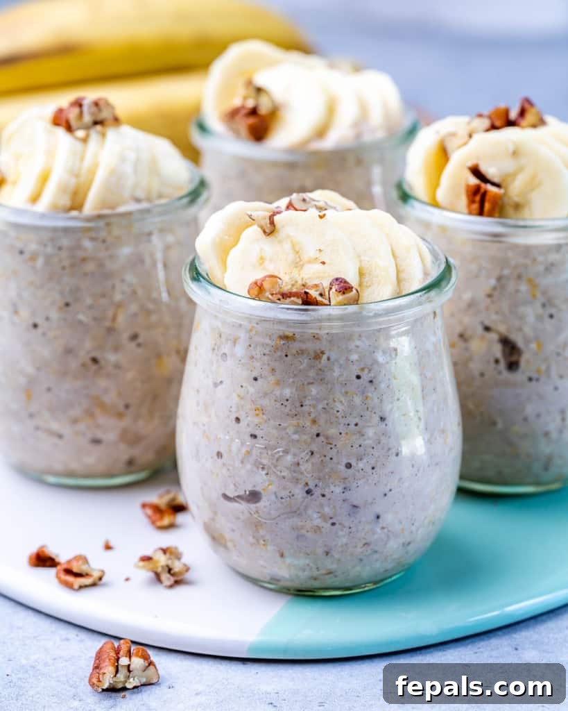 No-Bake Banana Bread Oats 2 Four glass jars filled with creamy banana bread overnight oats, beautifully garnished with fresh banana slices and crunchy pecans on a wooden board.