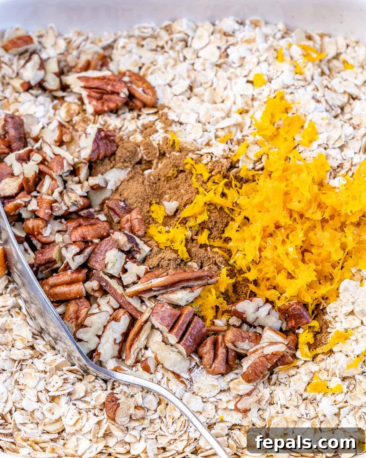 No-Bake Banana Bread Oats 5 A clear mixing bowl capturing the moment when old-fashioned oats, milk, mashed bananas, chopped pecans, orange zest, maple syrup, and cinnamon are being vigorously stirred together with a spoon until fully combined.