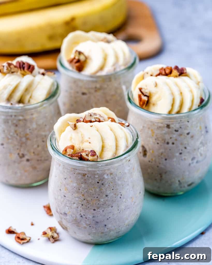 No-Bake Banana Bread Oats 7 Four pristine glass jars brimming with banana bread overnight oats, artfully topped with fresh banana slices and crunchy pecans, arranged on a rustic wooden surface in natural light.