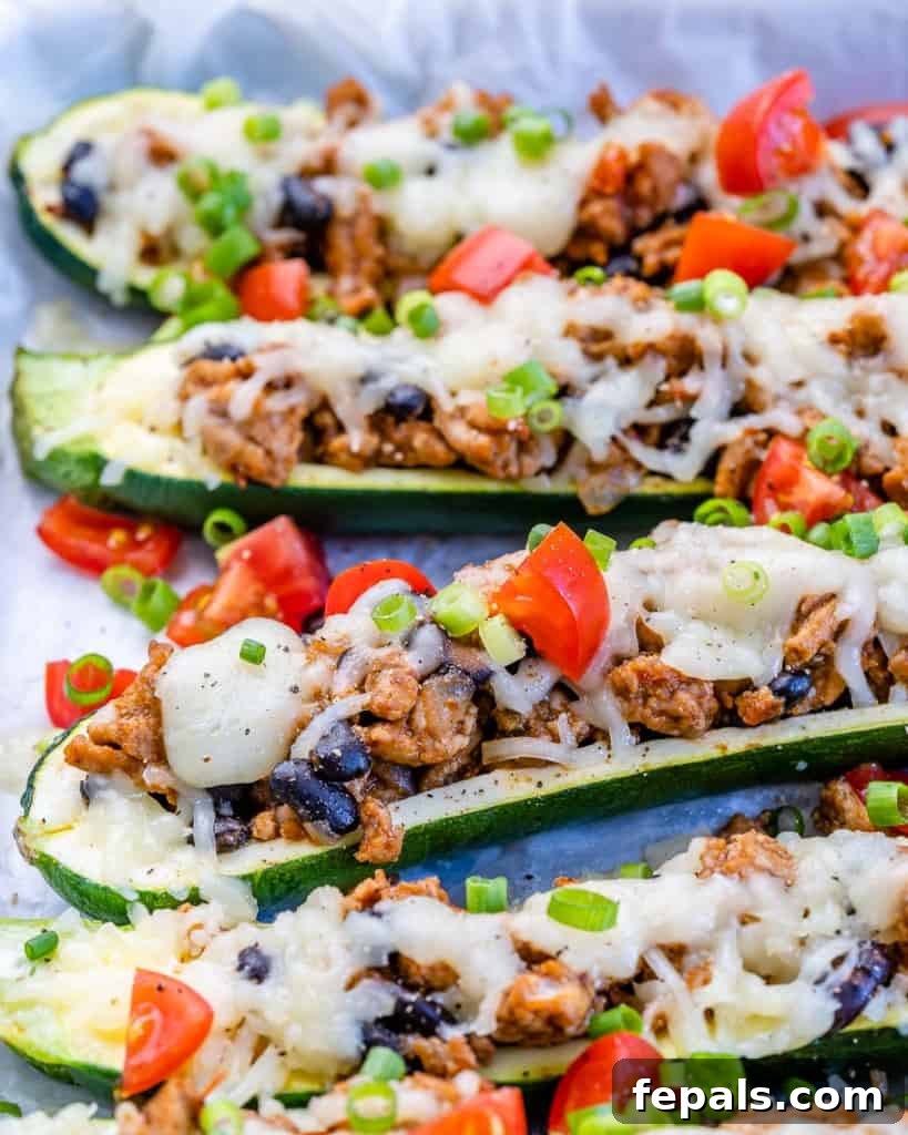 Side view of perfectly baked Taco Stuffed Zucchini Boats, generously topped with melted cheese and fresh, vibrant chopped tomatoes.
