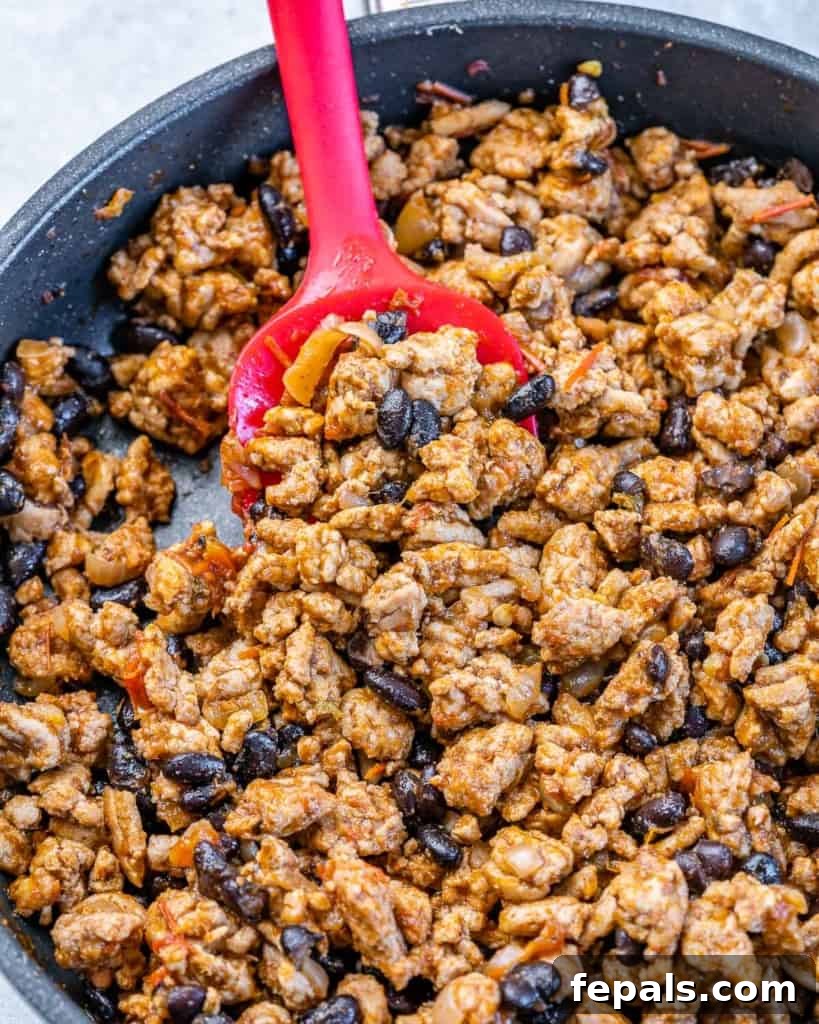 Rich and savory taco stuffing simmering in a skillet, stirred with a red spoon, ready to fill the zucchini boats.