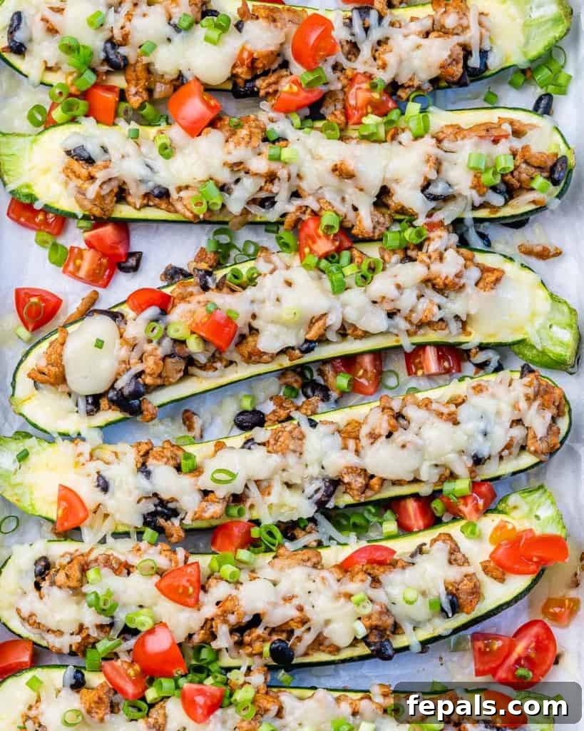 Close-up top view of freshly baked Taco Stuffed Zucchini Boats, adorned with perfectly melted cheese and finely chopped tomatoes.