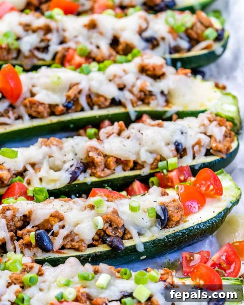 A delectable side view of freshly baked Taco Stuffed Zucchini Boats, featuring perfectly melted cheese and a sprinkle of chopped tomatoes.