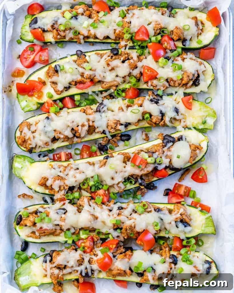 An inviting top view of freshly prepared Taco Stuffed Zucchini Boats, generously topped with melted cheese and vibrant chopped tomatoes.