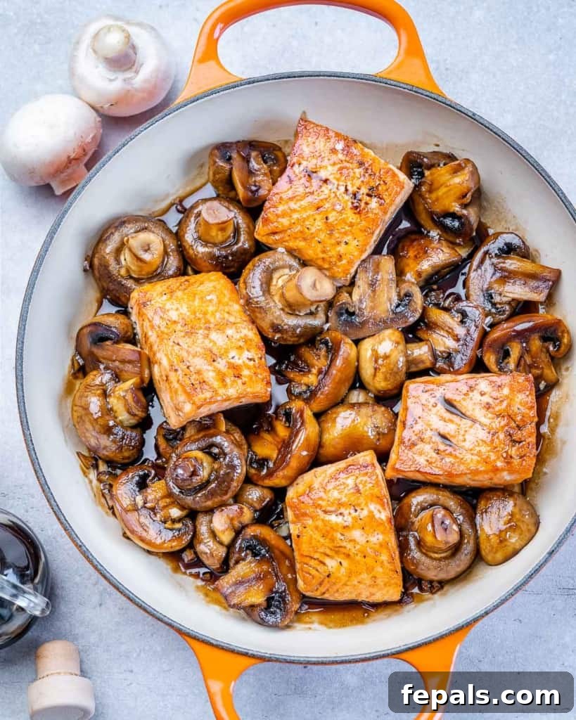 Close-up of skillet with honey balsamic glazed salmon and mushrooms, garnished with fresh herbs.