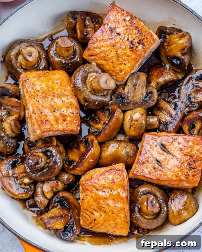 Top-down view of a vibrant honey balsamic glazed salmon with sautéed mushrooms in a cast iron skillet.
