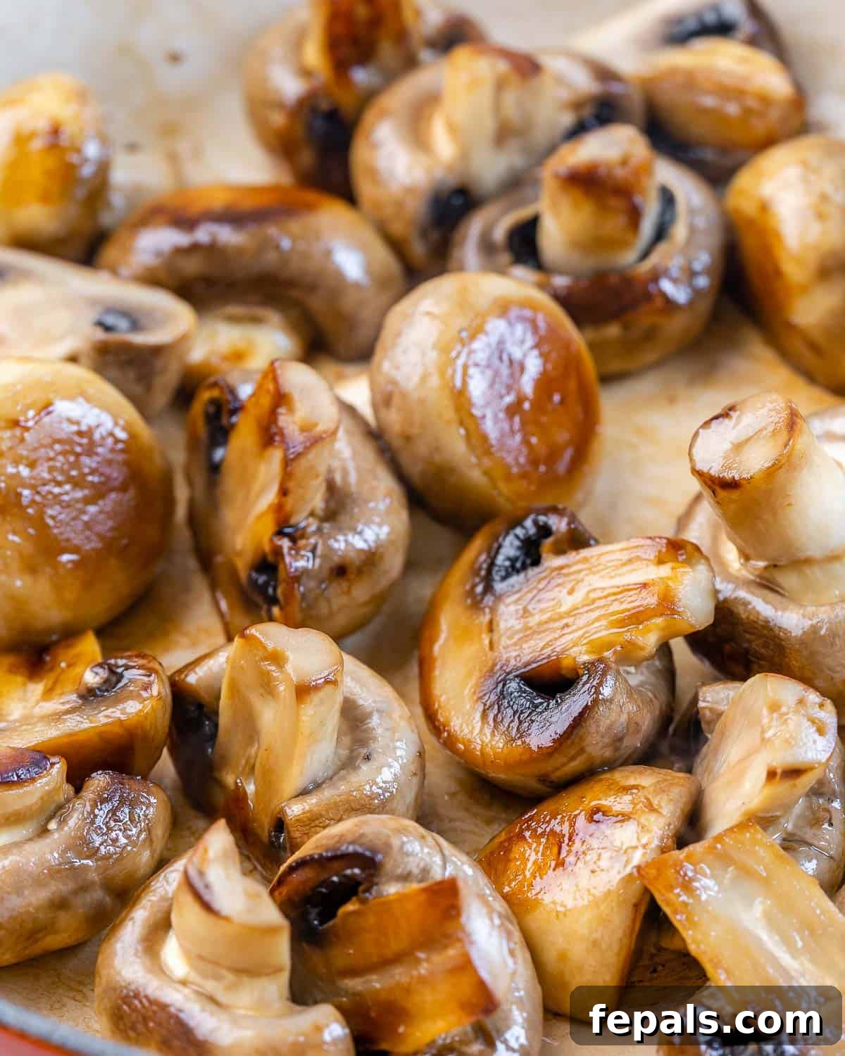 Halved button mushrooms sautéing in a skillet, with the honey balsamic glaze being poured over them.