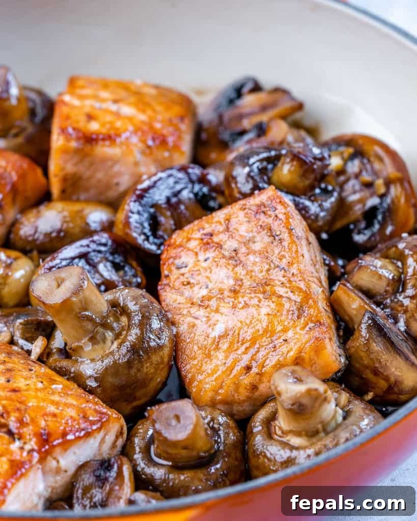 Front view of a single honey balsamic glazed salmon fillet served over a bed of sautéed mushrooms in a skillet, garnished with fresh parsley.