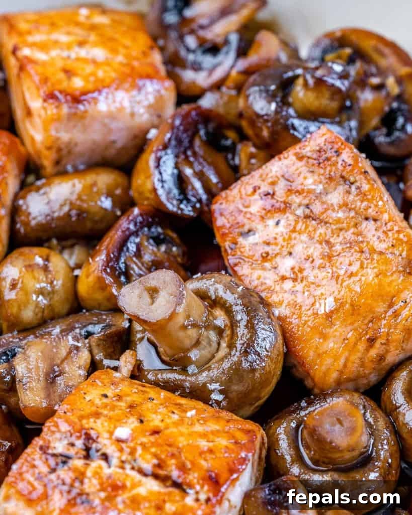 Close-up view of honey balsamic glazed salmon, highlighting the flaky texture and glossy glaze, with mushrooms in the background.