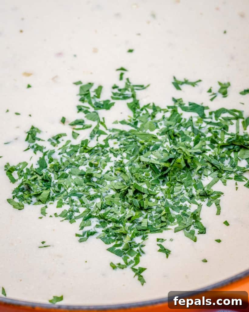 Ultimate Creamy Garlic Chicken Skillet 6 A hand gently sprinkling vibrant fresh parsley over a skillet of creamy garlic chicken, enhancing its aroma and visual appeal.