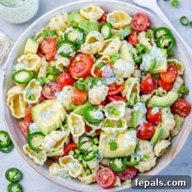 pasta salad in a white bowl with tomato and sliced avocado.