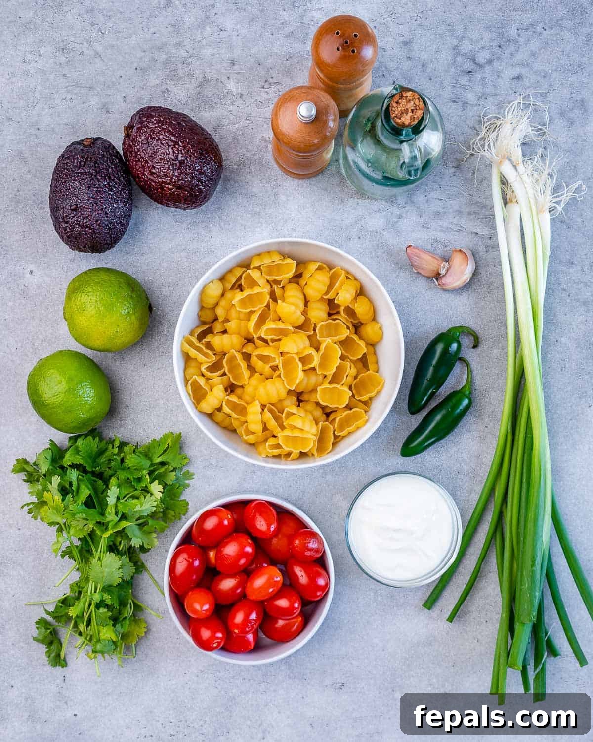pasta, Greek yogurt, green onions, jalapeño peppers, garlic cloves, salt, pepper, avocados, limes, cilantro, and cherry tomatoes for pasta salad