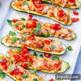 Zucchini Enchilada Bake 11 Top view of zucchini boats topped with chopped tomatoes, on a white plate.