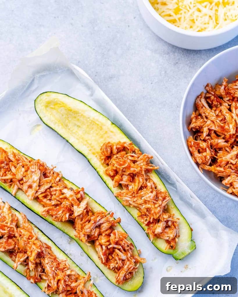 Zucchini Enchilada Bake 6 Hands filling zucchini halves with a mixture of shredded chicken and sauce.