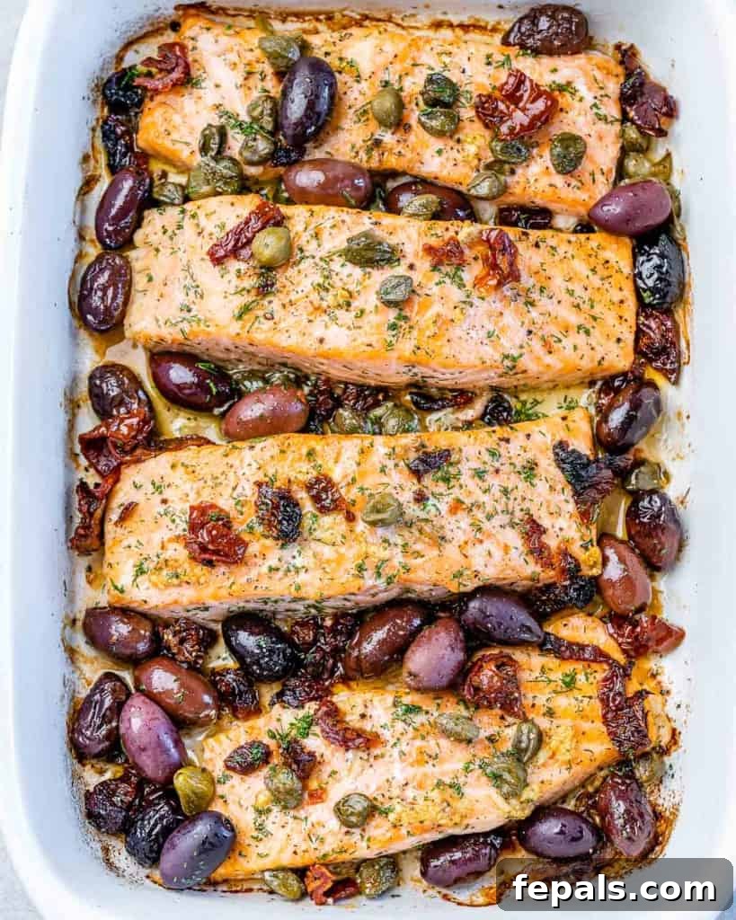 top view baked salmon in a white baking dish, topped with olives