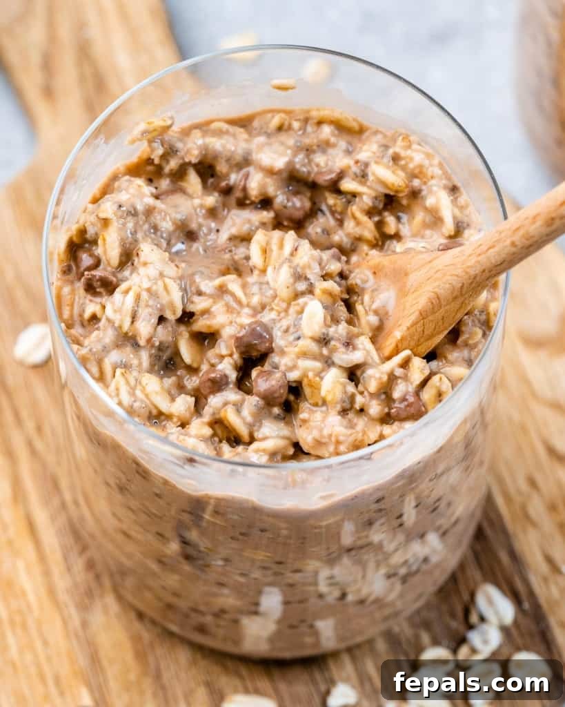 Guilt-Free Cookie Dough Oats 3 Kremalı kurabiye hamuru geceden kalma yulafla dolu bir cam kavanozda kaşık, tüketilmeye hazır.