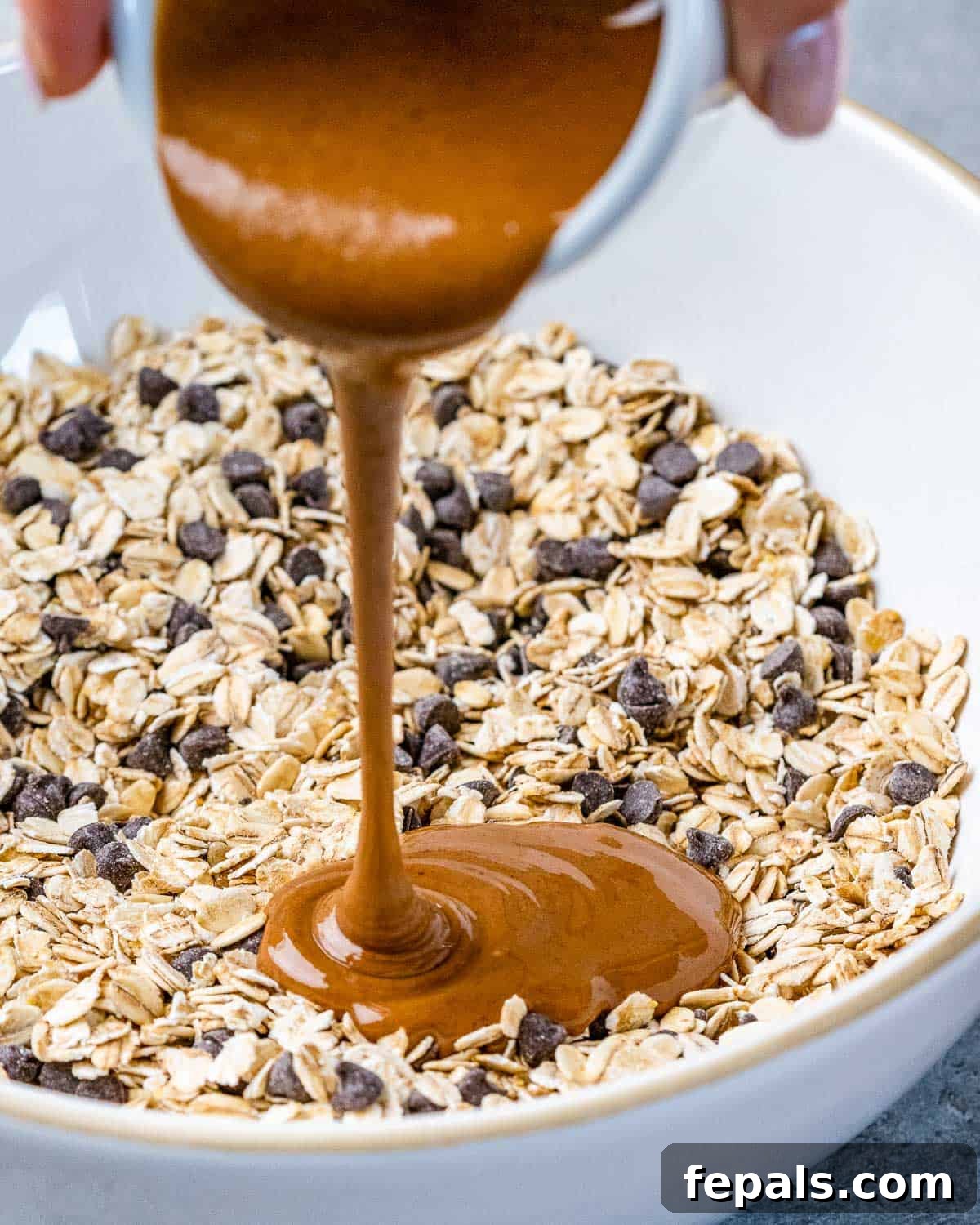 Guilt-Free Cookie Dough Oats 6 Kremalı badem ezmesi kuru yulaf karışımına bir kaseye dökülüyor.