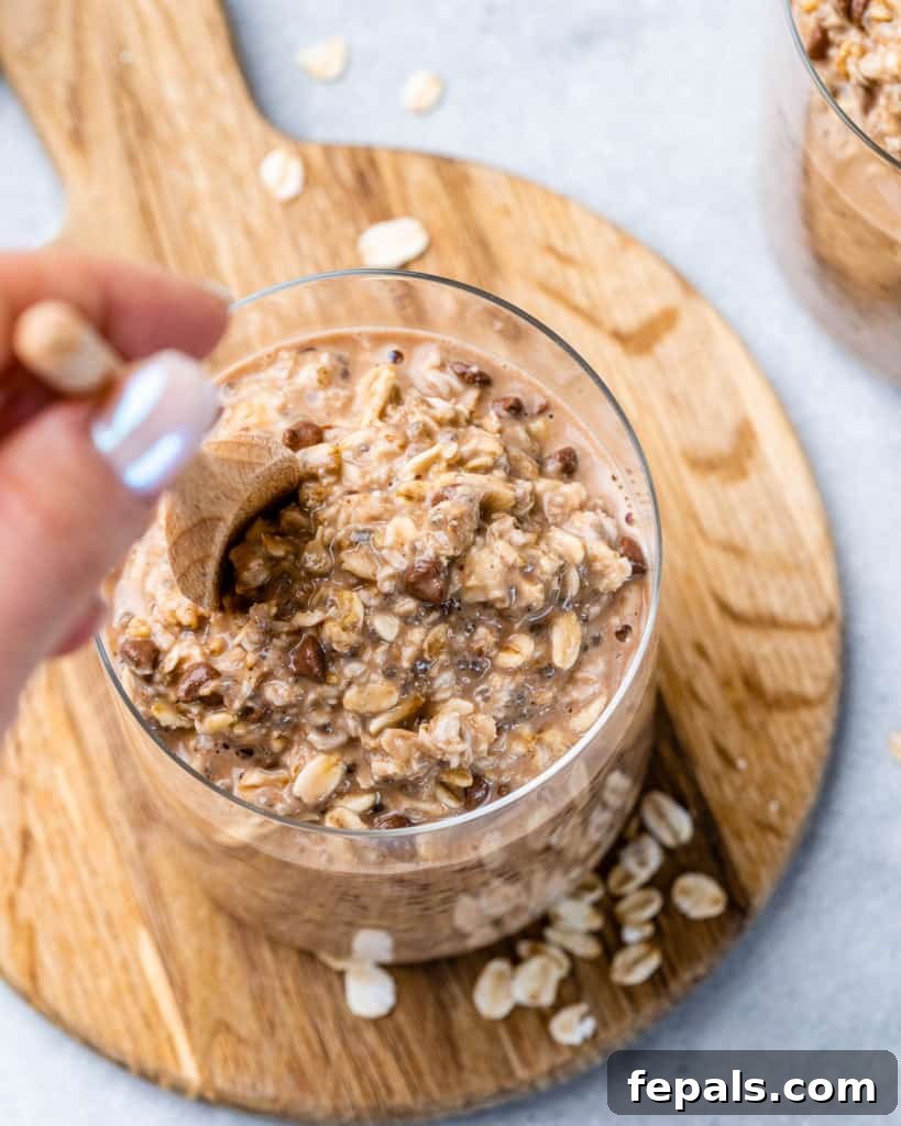Guilt-Free Cookie Dough Oats 8 Bir kadının eli, bir kavanozdaki mükemmel ıslanmış geceden kalma yulafı kaşıkla karıştırıyor, tüketilmeye hazır olduğunu gösteriyor.