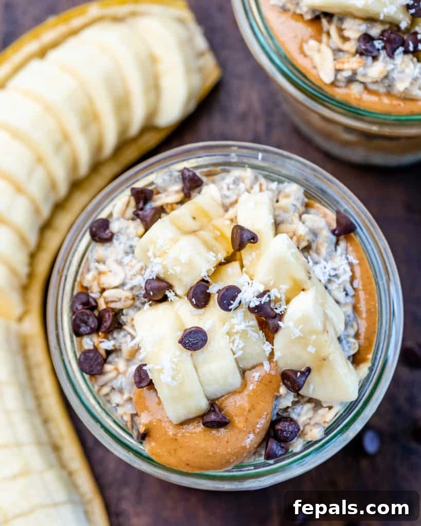 Overhead view of two jars of overnight oats topped with banana slices, peanut butter drizzle, and mini chocolate chips.