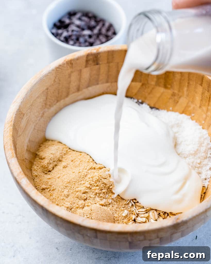 Pouring coconut milk into a bowl with oats, chia seeds, and shredded coconut.