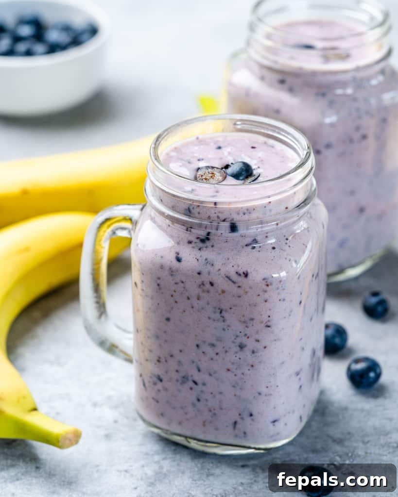 A refreshing blueberry banana smoothie, served in a clear mason jar with a straw, garnished with a few fresh blueberries on the side.