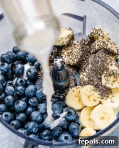 Pouring milk into a blender with blueberries, bananas and chia seeds.